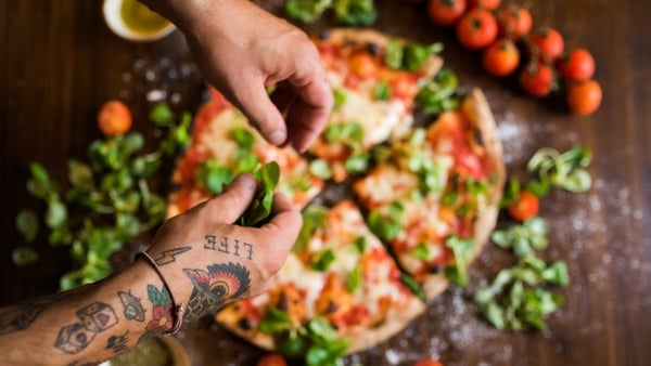 Close up of tattooed hands making pizza with basil