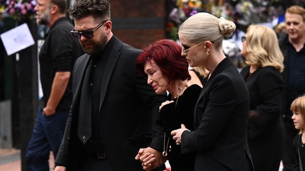 (L-R) Jack Osbourne, Sharon Osbourne, and Kelly Osbourne view tributes to the late Ozzy Osbourne from fans as his funeral cortège travels through his home city of Birmingham on 30 July, 2025