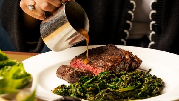 a person pouring sauce on a plate of meat