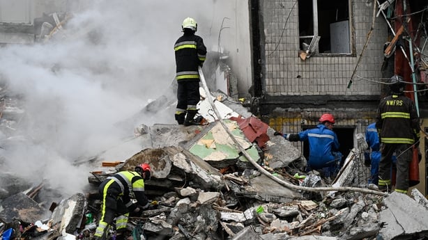 a group of firefighters in Kyiv working on remains of a residential building which is left in rubble with smoke billowing