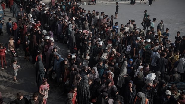 Hundreds of people holding empty pots wait in line for food in Gaza City