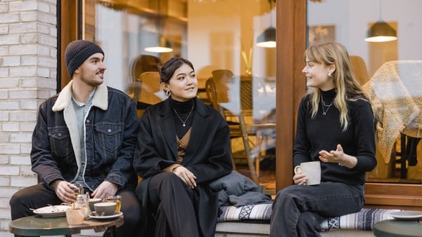 Three friends sitting at street cafe talking while having coffee. Group of young people sitting outside a cafe.