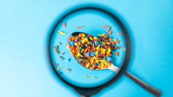 Microplastic pieces on spoon under magnifying glass on blue background