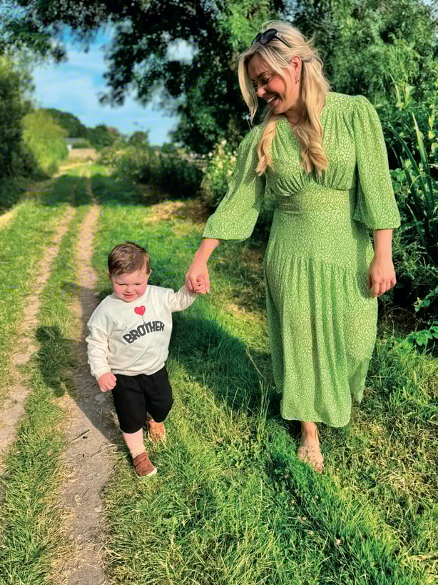 a woman in a green dress and child walking on a grassy path