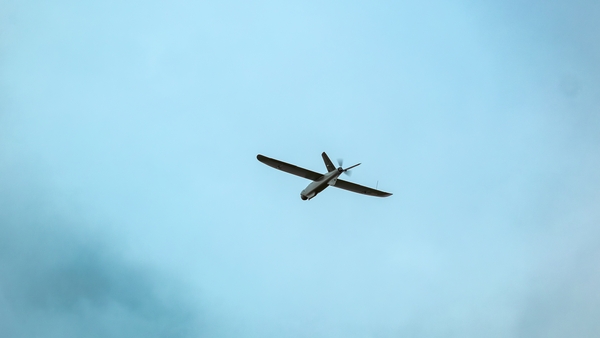 A drone flies against a bright blue sky with scattered clouds (stock pic)