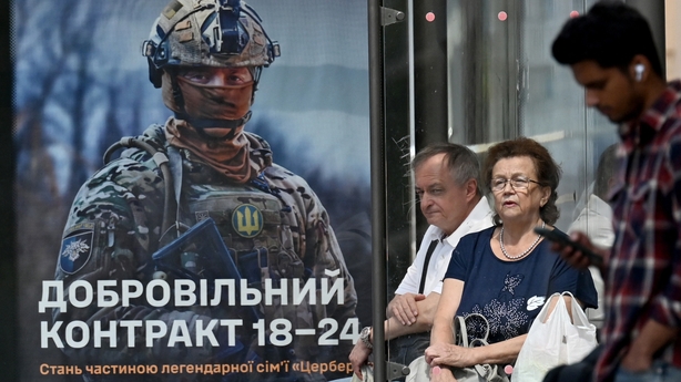 People wait at a bus stop next to a recruitment advert of the Ukrainian Armed Forces in Kyiv