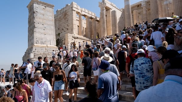 Thousands of tourists wear hats and carry umbrellas for protection as they visit the Acropolis in Athens