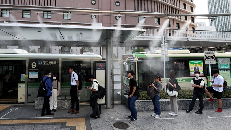Commuters wait for a bus under a water mist spray in the Umeda district of Osaka, Japan, amid high temperatures