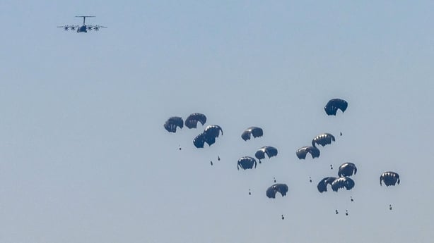 A plane is seen in the sky dropping boxes of aid with parachutes for people in Gaza