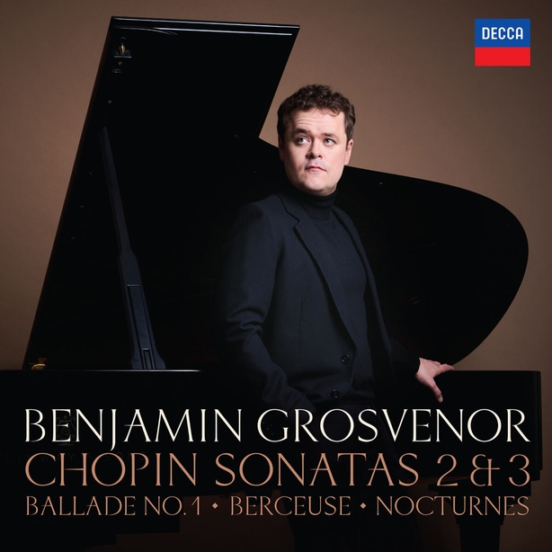 Benjamin Grosvenor in black standing in front of a baby grand piano