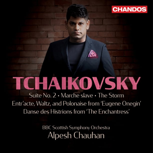 Alpesh Chauhan in a black suite with a pink pocket square standing in front of a brick wall