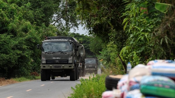 A military truck is driving down a road surrounded by leafy trees