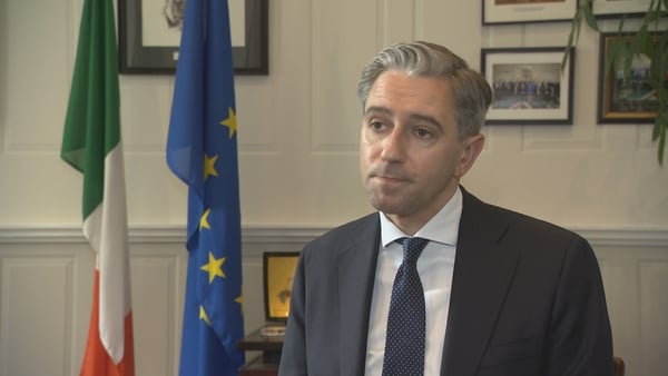 Simon Harris sitting down in his office with the Irish and EU flags behind him
