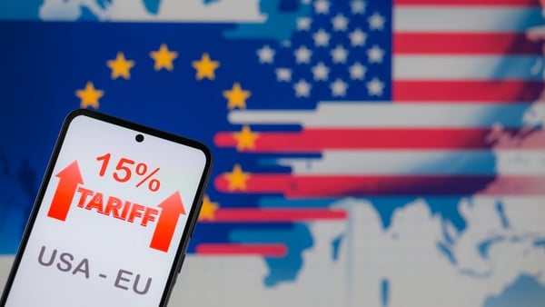 A mobile phone shows the 15% tariff in front of a graphic depicting the eu and us flags