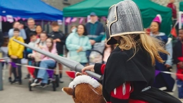 A little girl dressed as a knight charges on a toy horse.