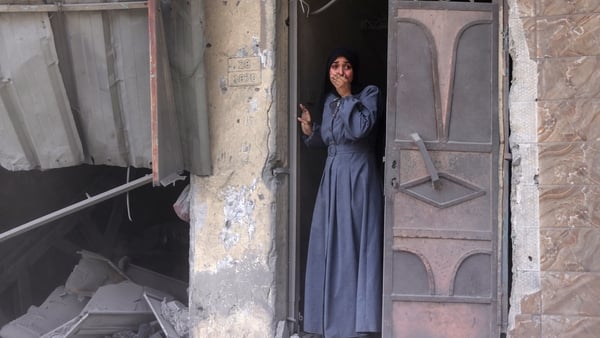 A tearful Palestinian woman standing in a doorway with her hand in her mouth as she watches the aftermath of an Israeli strike that hit Gaza City's southern al-Zeitoun neighbourhood