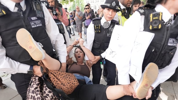 Four police officers carry a woman by her arms and legs in London