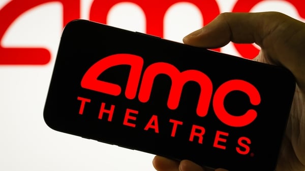 A person holds a smartphone with the logo of AMC Entertainment Holdings in red