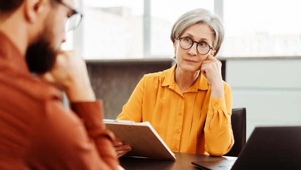 Older woman wearing yellow shirt talking to a younger colleague in an office