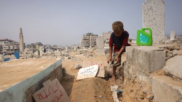 A Palestinian boy adjusts stones around the grave of Al Jazeera correspondent Anas al-Sharif