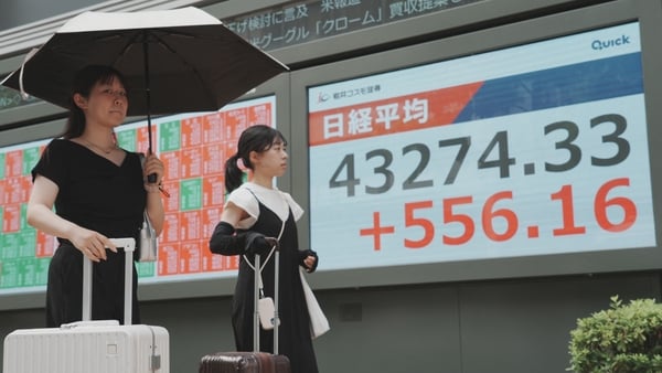 Pedestrians walk in front of an electronic quotation board displaying the Nikkei Stock Average on the Tokyo Stock Exchange in Tokyo