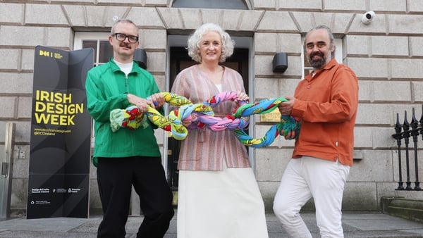 A group of people holding a chain of claddagh scarves outside a building with an Irish Design Week banner outside it