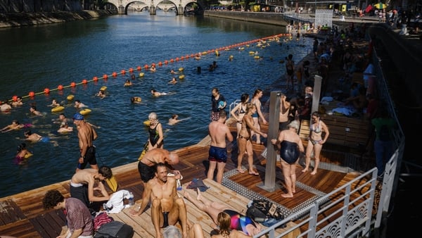 People are standing on a pier using showers and waiting to get into the water where people are seen swimming