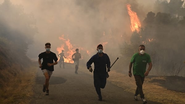 People run by a burnt area during a wildfire near the village of Larouco, in the province of Ourense, in northwestern Spain