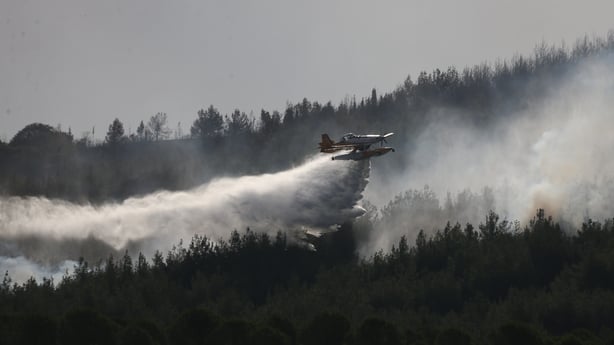 A plane drops water to put out the fire as smoke from the fire area fills the sky while firefighters and Turkish General Directorate of Forestry teams continue their efforts to extinguish the fire