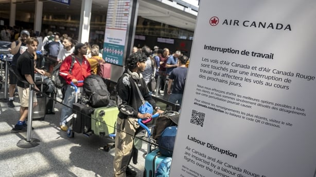 Air Canada passengers wait in line in an airport with a strike notice in front of them in both English and French 