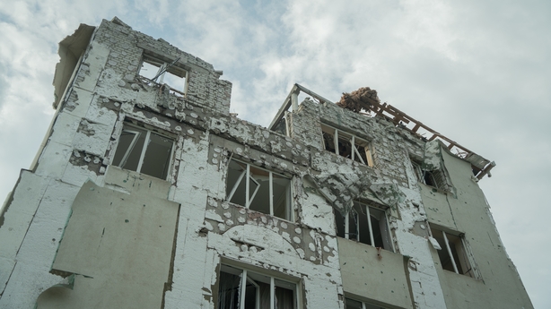 A white apartment building is seen heavily damaged with missing windows and a portion of the building missing after a drone attack