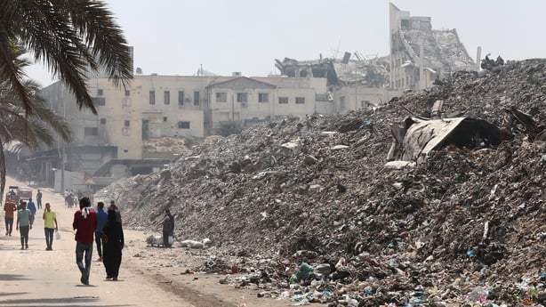 Palestinians walk past piles of waste on the roadside in Gaza City 