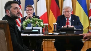 Volodymyr Zelensky sits while staring off camera and Emmanuel Macron and Donald Trump stare towards camera with a variety of European flags in the background