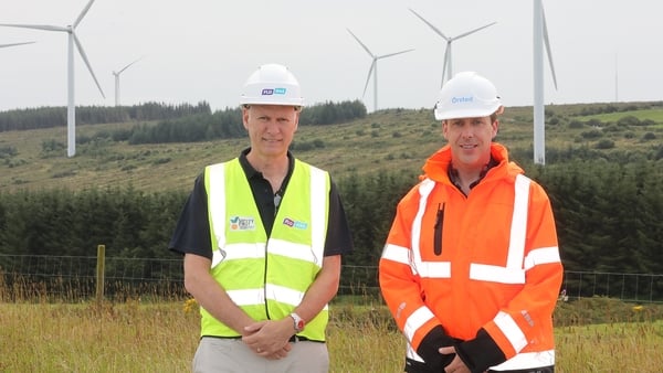 Two men in high viz jackets stand in front of wind turbines