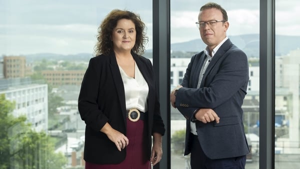 A woman and a man pose for a photo at the window of a high rise office