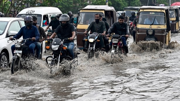 Commuters wade through a flooded street after heavy rainfall in Karachi, Pakistan