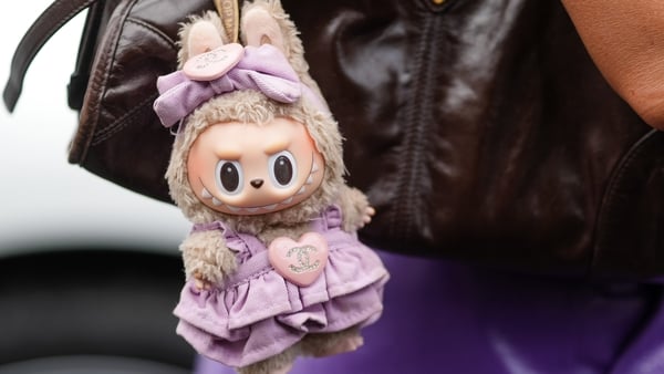 A woman walking wit aLabubu doll attached to her handbag