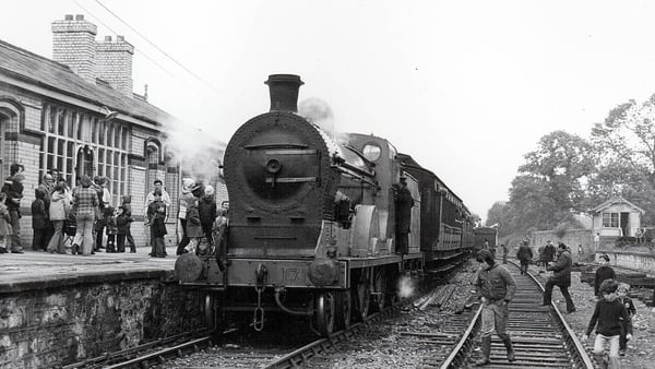 A steam train with passengers milling around