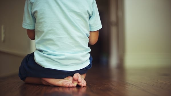 small boy kneeling while showing back to camera with visible feet.