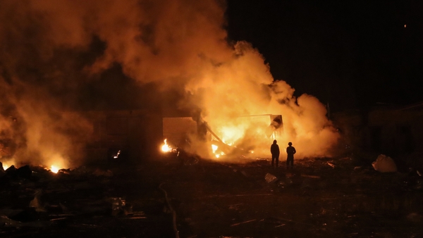 People stand in front of burning building at residential district after Russian drone attack on Okhtyrka, Ukraine