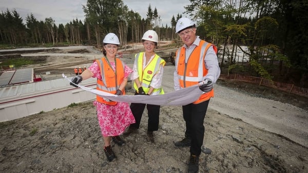 2 women and a man in high vis vests looking at construction plans with trees in the background