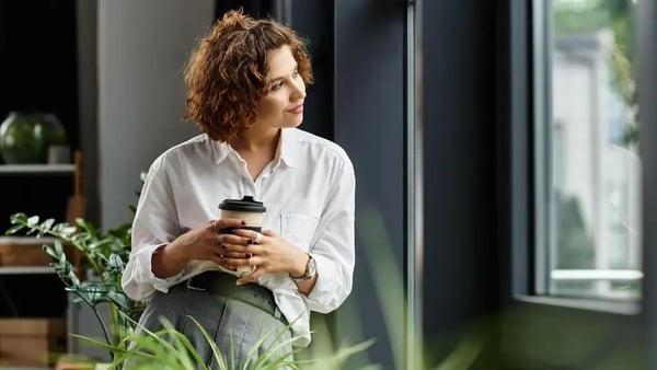 Professional woman looking out a window, drinking a coffee