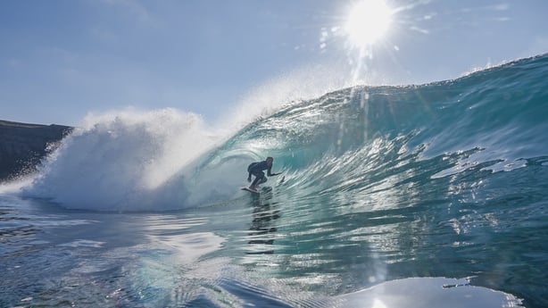 A young boy surfing on a wave with the sun in the background.