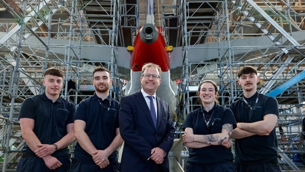 Young apprentices pose under the tail of an airplane with Minister James Lawless in the centre.