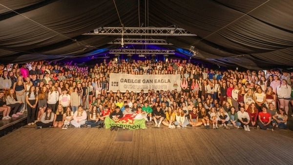 Students gather in a concert hall and hold a sign in both Irish and Welsh