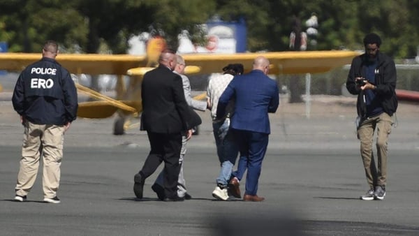 Four men surround a fifth man while a photographer takes photos