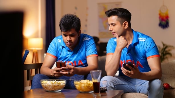 Indian men watching online live cricket match on an app in a sitting room