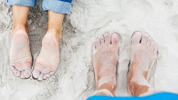 Close up of two pairs of feet covered in sand on a beach