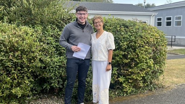 Student Rónán Ó hÍcí poses holding his Leaving Cert Results standing beside teacher Eibhlín Uí Chonchubhair.