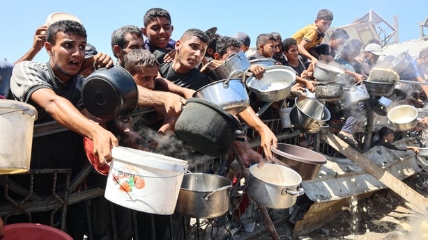 Several people with pots and pans reach out in an attempt to receive food